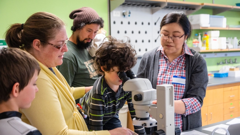 a woman scientist showing two boys and their parents how to use a microscope.